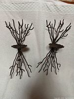 Photo showing pair of twisted iron wall sconces against a white quilted background, displaying their shape and size.