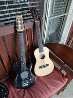 Front view of black electric and natural acoustic guitars side by side on chair.