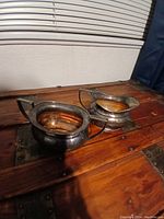 Photograph of two heavy silver plated vessels on wooden surface, showing their rounded shape and patina.