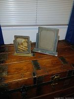 Two antique Art Deco swinging picture frames on wooden surface, showing size difference and aged condition.