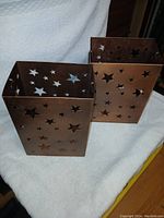 Front and side view of two rectangular rustic tin candle holders with star cutouts.