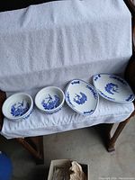 Four pieces of blue and white china laid side by side on a white towel on a bench, showing two bowls and two oval dishes