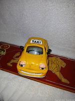 Front view of vintage yellow Chevron collectible toy taxi car with eyes and smile on front, TAXI sign on roof.