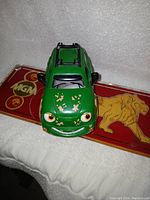 Top front angle view of green vintage Chevron toy car with face and paint wear.