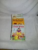 Photo showing three vintage Little Golden Books stacked with covers partially visible: 'Four Puppies', 'Old MacDonald Had a Farm', and 'Snow White and the Seven Dwarfs'.