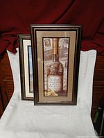 Two framed prints, one featuring a Château de la Côte 1978 vintage wine bottle image, the other a lighthouse on the coast.