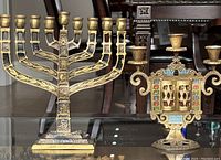 Overview of both brass menorah and enamel candelabra on glass table