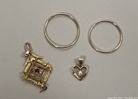 Photo showing 14K gold hoop earrings and two 10K gold pendants, one square-shaped with red crystal and one heart-shaped with a pearl