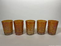 Front view of five marigold carnival glass tumbler glasses showing detailed embossed windmill design.