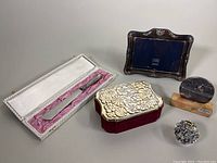 Full view of all five sterling silver items including photo frame, trinket box, cutting utensil, floral item, and oval mounted item.
