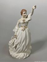 Front view of porcelain figurine showing detailed white dress with gold accents, woman holding fan and raising one arm.