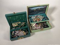 Two open jewelry boxes filled with costume jewelry piled in trays and bottoms