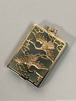 Close-up of the jade pendant showing gold-toned crane decoration and cloud motifs, angled to highlight texture and detail.