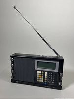 Front-angle view of the Grundig Satellit 500 portable AM/FM shortwave radio with extended antenna, showing speaker, LCD screen, and keypad.