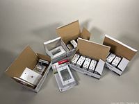 Open boxes containing white tamper-resistant electrical receptacles, white wall plates, and one box containing various electrical parts.