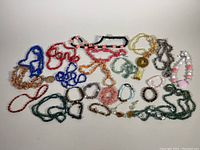 Top-down view of assorted semi-precious stone necklaces and bracelets laid out on a white background showing various colors and styles
