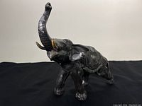 Front angled view of black cast metal elephant with raised trunk and chipped paint showing metal underneath, displaying overall shape and condition.
