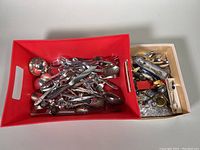 Two boxes containing a large assortment of vintage serving spoons, ladles, salad tongs and cutlery items in varied condition, seen from above.