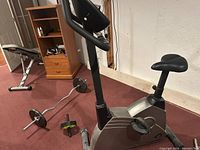 Photo of stationary exercise bike with adjustable seat and black handles, showing the body, seat, handles, and pedals.