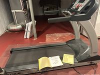 Full side view of True treadmill showing running deck, base, and manual on top.