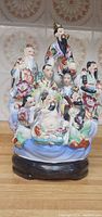 Photo of colorful porcelain sculpture with three main figures and several smaller surrounding figures on wooden base.