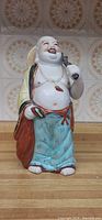 Photo of a porcelain Buddha sculpture holding an umbrella, displaying its front view and colorful robes.