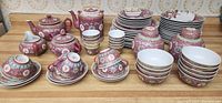 Full overview of the red porcelain chinaware pieces arranged showing teapots, cups, saucers, bowls, plates, and spoons.