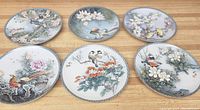 Six imperial Jingdezhen porcelain plates arranged flat, featuring detailed bird and flower designs, showing the range of artistic motifs across the set.