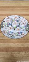 Photo of the hand-painted decorative porcelain plate displaying multiple floral designs and Chinese characters with six matching floral porcelain cups arranged upside down on the plate.