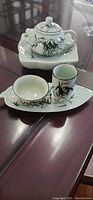 Photo of small green porcelain tea set including teapot with lid on a stand, cup, and bowl with bamboo design