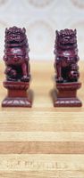 Pair of red wooden lion bookends on wooden surface with wallpaper background, showing detailed facial carving and polished finish.