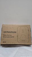 Closed cardboard box labeled 'Cell Phone Booster' with text 'Raise the bar, boost your world!'.