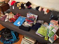 Large assortment of ladies hats, gloves, scarves, t-shirts, pantyhose, and sports bags arranged on a couch and floor.