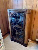 Front angled view of vintage Art Deco wooden display cabinet with glass door and grille.