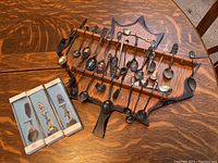 Overall collection of about 18 collectors spoons mounted on a decorative wooden spoon holder on a wood table, with three boxed BMCO Sterling spoons nearby.