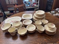 Wide view of most porcelain items on table showing stacks of plates, bowls, cups, and saucers.