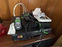 Sony SLV-N60 VCR and LG BP350 Blu-ray player stacked on wooden surface with remotes and cables on top, showing front panels and connections