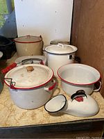 Photo showing six enamelware items: three lidded pots, chamber pot, bedpan, and female urinal on a shelf.