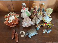 Photo showing full lot with ceramic cuckoo clock, several vintage figurines including a girl in frilly dress, cat, and small ceramic animals