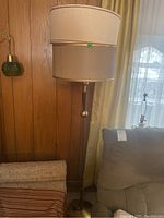 Full view of the assembled MCM floor lamp showing dual paper lampshades (one beige shade on bottom with visible damage, and one white shade on top), metal stand, wood accents, and brass-colored ball ornament.