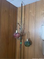 Full view of brass-tone pole lamp with two of three glass globes visible (red and green) against wood paneling.