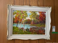 Framed painting showing full artwork of an autumn lakeside scene with birch trees and a wooden fence, white ornamental frame.