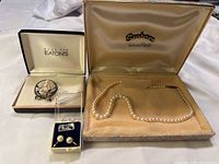 Lot includes a pearl necklace in a box labeled 'Scaharn Cultured Pearls', a circular sterling silver pin with three cultured pearls in a box labeled 'Made for Eaton's', and a small box containing pearl screw back earrings.