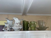 Wide view of all six pitchers lined up, three porcelain with floral designs on the left and three green and clear glass pitchers on the right with matching glass bowl
