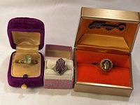 Three rings in presentation boxes: green, purple, grey cat’s-eye designs