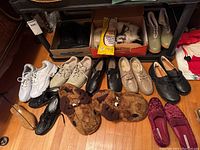 Overview of all shoes and boots arranged on wooden floor including sneakers, slippers, and various casual and dress footwear.