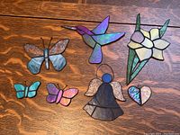Full set of 7 stained glass pieces displayed on wood surface including butterflies, hummingbird, flower, angel and heart shapes.