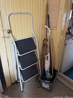 Three-step metal ladder and bucket of cleaning tools against yellow wall