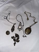 Image showing 5 pieces of sterling silver jewelry including two pendants with stones, an oval locket, and two brooches on white fabric