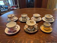 Six china teacups and six matching saucers arranged on a wooden table, showing the variety of floral patterns and colors